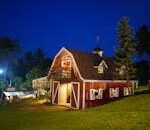 pexels photo 3025117 3025117 A charming red barn with lights surrounded by lush greenery under a clear night sky.